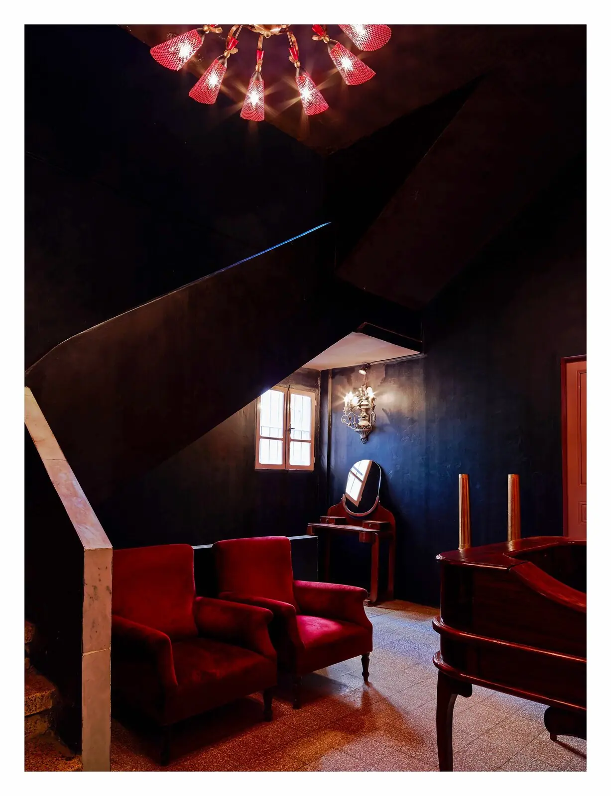 Boudoir aux fauteuils de velours rouge et lustre, sous l'escalier