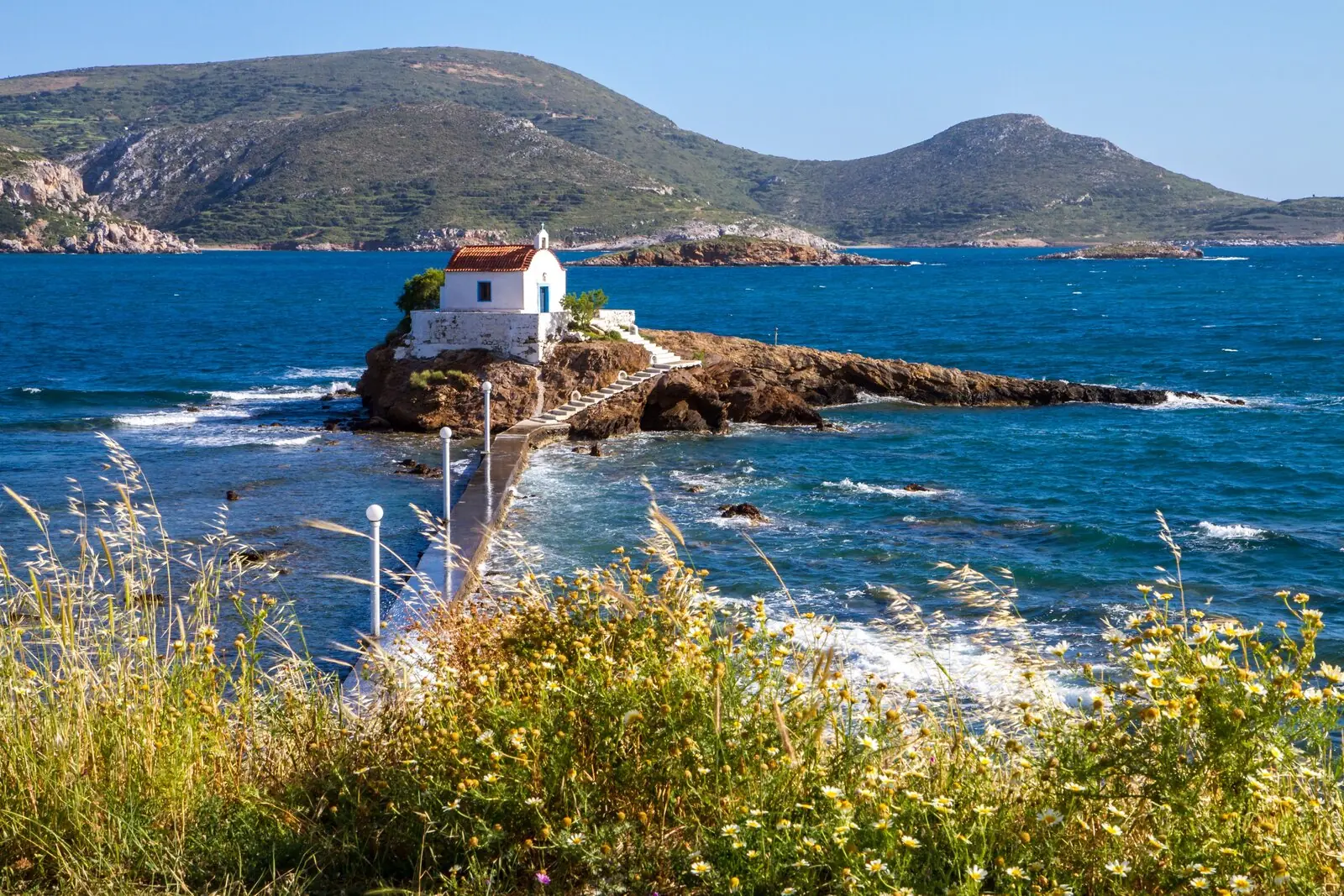 La chapelle Agios Isidoros reliée à la côte par une digue, parmi les fleurs sauvages